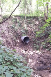 Once completely encased in its embankment, this 30-inch diameter culvert hangs suspended after rainwater flood runoff plugged it, flowed over the driveway above it, and washed away more than two feet of the bank.  